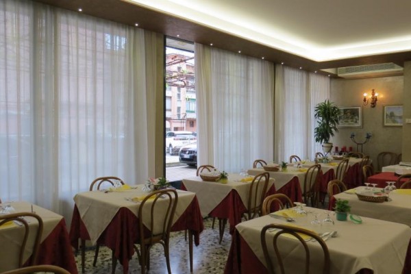 Restaurace s prostřenými stoly, červenými ubrousky a dřevěnými židlemi u velkých oken.