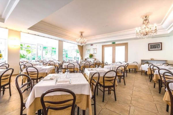 Světlá restaurace s prostřenými stoly a dřevěnými židlemi.
