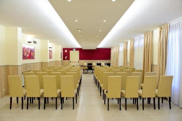 Konferenční místnost s řadami béžových židlí a prázdnou tabulí vpředu.