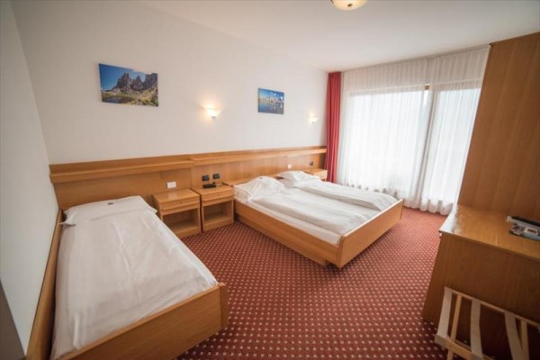 Dvojlůžkový pokoj s oddělenými postelemi, dřevěným nábytkem a velkým oknem s průsvitnými závěsy.