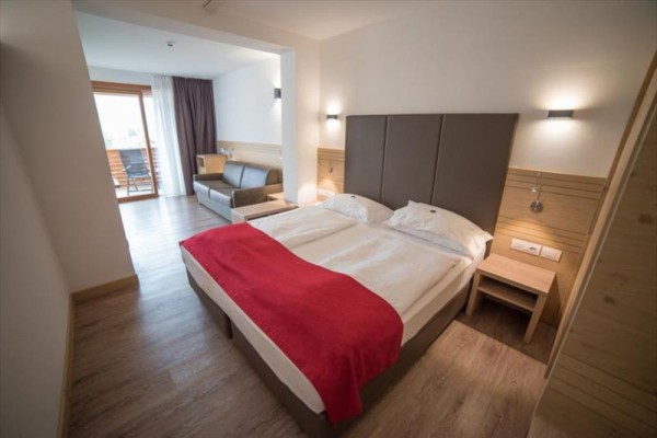 Moderní hotelový pokoj s manželskou postelí, pohovkou a balkonem s výhledem.
