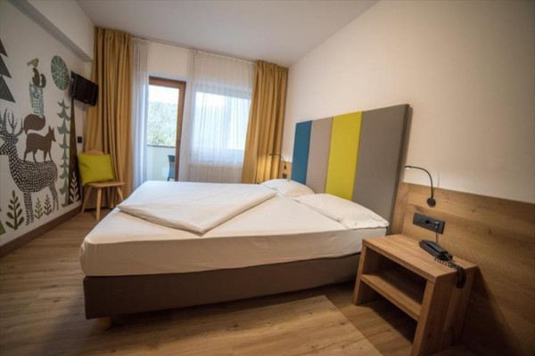Moderní hotelový pokoj s manželskou postelí, nočním stolkem a malbou zvířat na zdi.