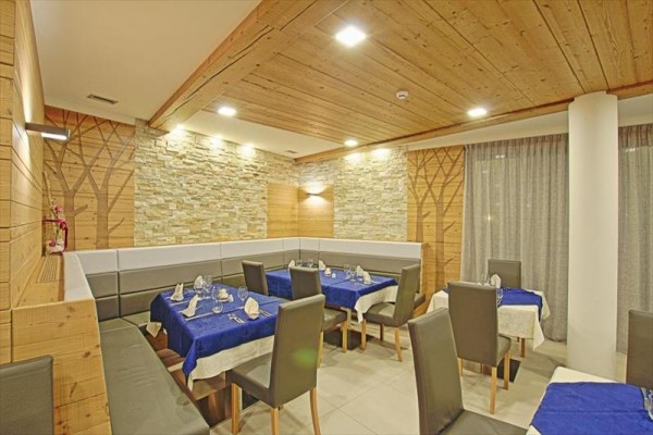 Restaurace s kamennými zdmi a dřevěným stropem, s modrými ubrusy a šedými židlemi.