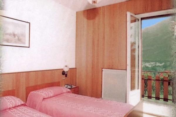 Dva růžově povlečené postele v pokoji s otevřenými dveřmi na balkon s výhledem do přírody.