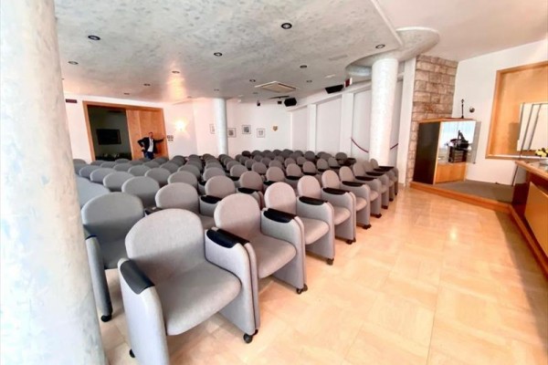 Prázdný konferenční sál s řadami šedých sedadel.