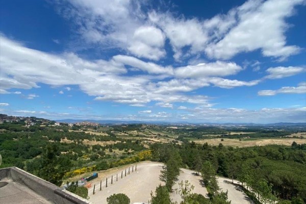Panoramatický výhled na krajinu s kopci, stromy a modrou oblohou s mraky.
