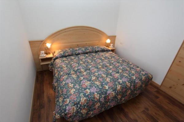 Dvoulůžková postel s květinovým povlečením a dvěma lampičkami na dřevěné čelní desce.