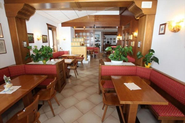Restaurace s dřevěným nábytkem a červenými lavicemi, ozdobené rostlinami.
