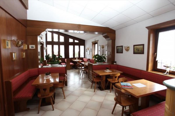 Interiér útulné restaurace s dřevěným nábytkem a červeným čalouněním.