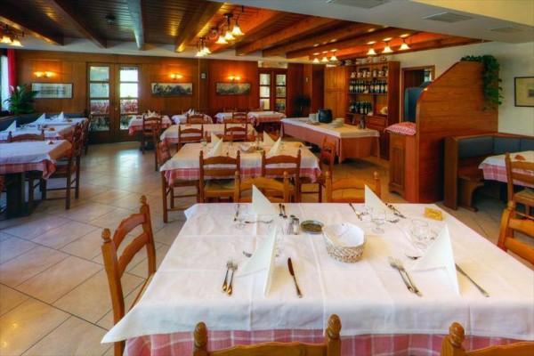 Restaurace s dřevěným nábytkem a prostřenými stoly s bílými ubrusy a ubrousky. 