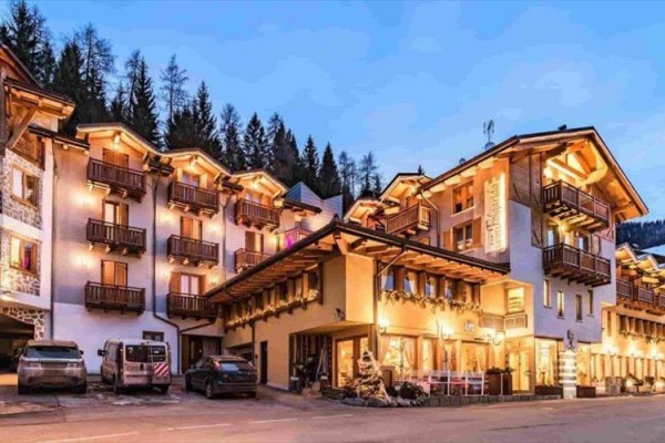 Horský hotel s dřevěnými balkony osvětlený v zimní krajině.