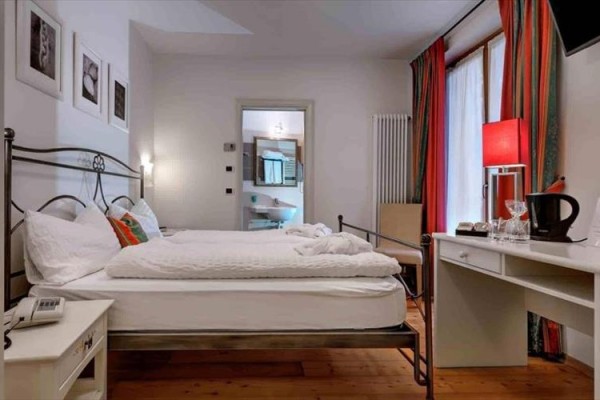 Elegantní ložnice s manželskou postelí, psacím stolem a otevřenou koupelnou v pozadí.