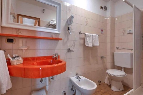 Koupelna s oranžovým umyvadlem, bidetem a toaletou.
