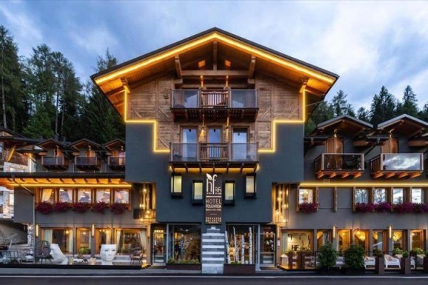 Horské budova hotelu s osvětlením a balkony, obklopená lesem.