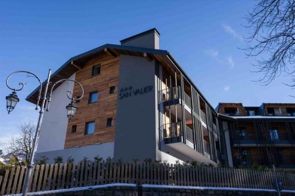Hotelová budova s dřevěnými prvky a nápisem San Valier, obklopená plotem.