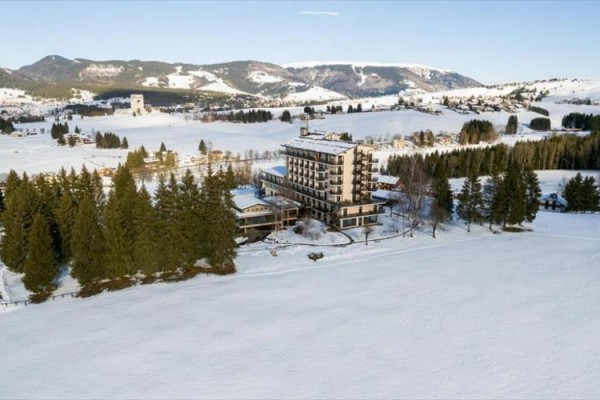 Horský hotel obklopený zasněženou krajinou a lesy.