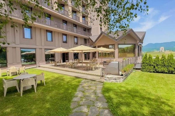 Terasa hotelu s posezením a slunečníky obklopená travnatým prostranstvím s výhledem na hory.