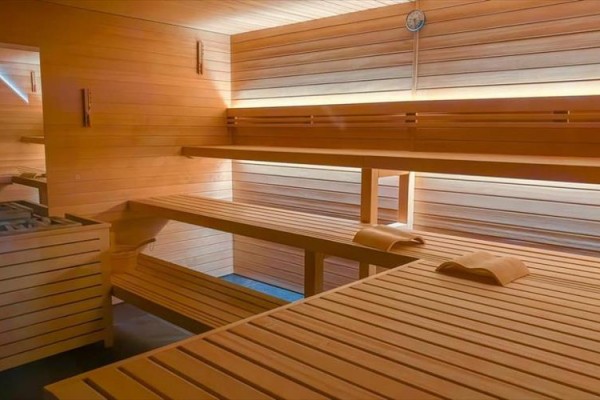 Dřevem obložená sauna s dřevěnými lavicemi a teploměrem na zdi.