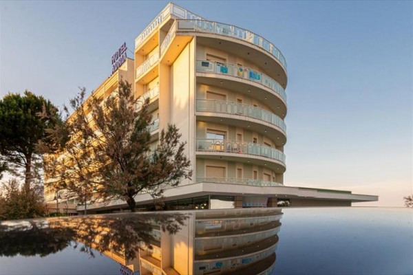 Moderní vícepodlažní budova hotelu s balkóny obklopená stromy za soumraku.