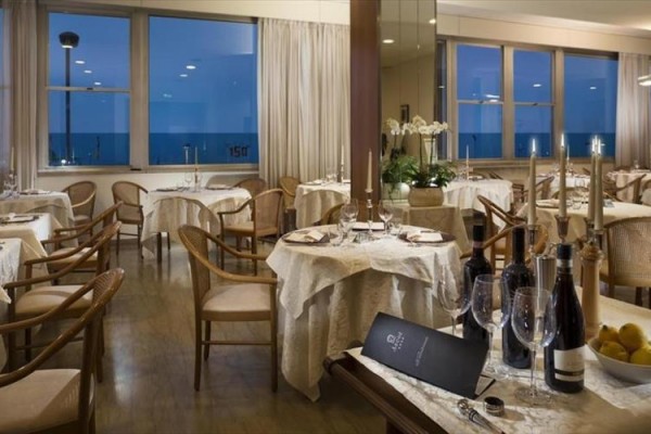 Elegantní restaurace s prostřenými stoly, láhvemi vína a výhledem na moře.