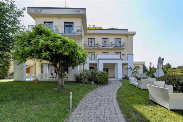 Třípatrová budova hotelu s terasou a zahradou s cestou a venkovním posezením.