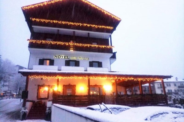 Třípatrový hotel ozdobený světelnými řetězy, zasněžená krajina.