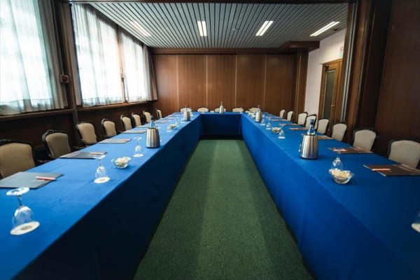 Konferenční místnost s uspořádáním stolu do tvaru písmene U s modrými ubrusy.