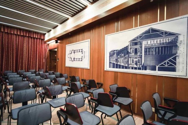 Místnost s řadami prázdných židlí a architektonickými plány na stěnách.