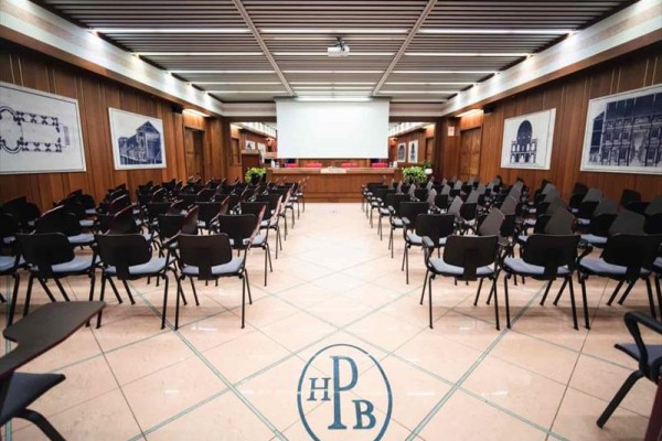 Konferenční místnost s promítací plátnem a pořadatelským stolem.