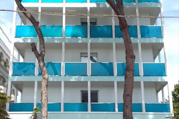 Moderní budova s modrobílými balkony a dvěma stromy v popředí.