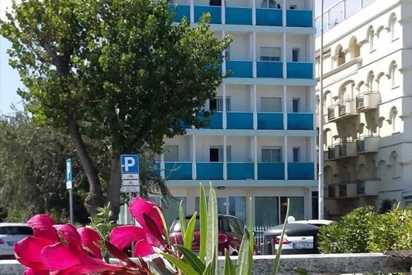 Čtyřpodlažní budova s modrými balkony a květinami v popředí.