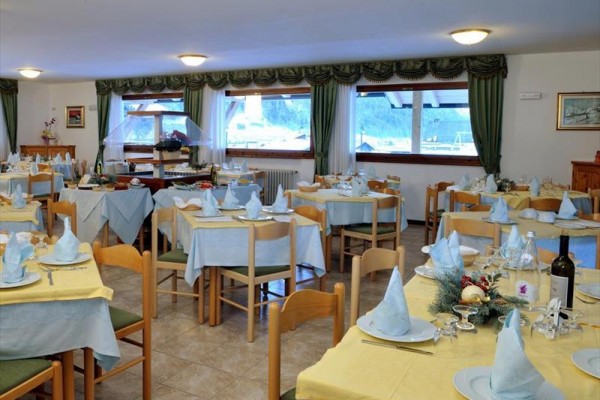 Prostorná restaurace s mnoha stoly připravenými pro hosty, ozdobená světle modrými a žlutými ubrusy.