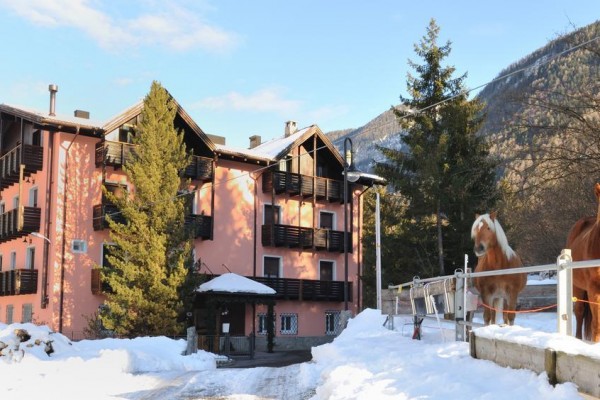 Růžový horský hotel se dvěma koňmi na zasněženém svahu.