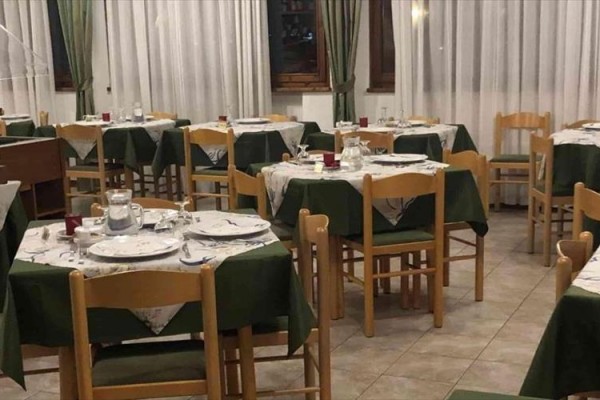 Restaurace s dřevěnými židlemi a zelenými ubrusy.