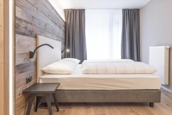 Moderní ložnice s dřevěnou stěnou, manželskou postelí a tmavými závěsy.
