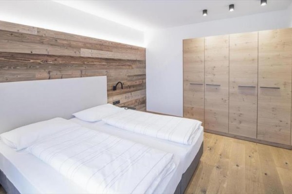 Moderní ložnice s manželskou postelí a dřevěnou šatní skříní.