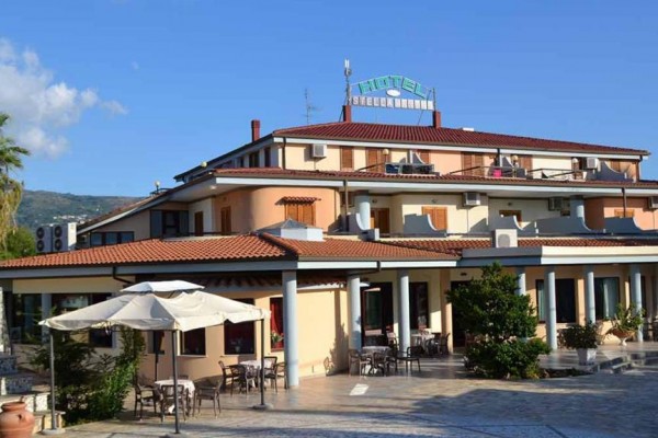 Hotel s terasou a venkovním posezením pod slunečníky.