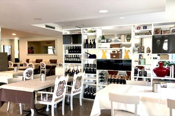 Stylová restaurace s bílým nábytkem a regály plnými lahví vína.