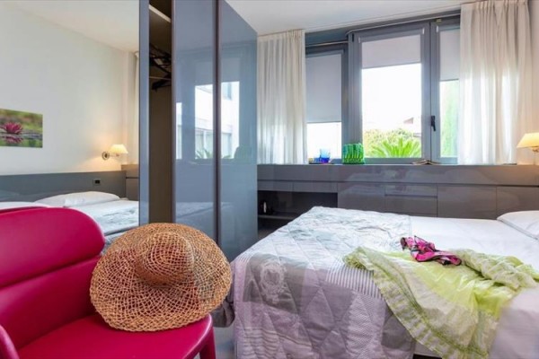 Moderní ložnice s dvojlůžkem, židlí s kloboukem a výhledem z okna.  