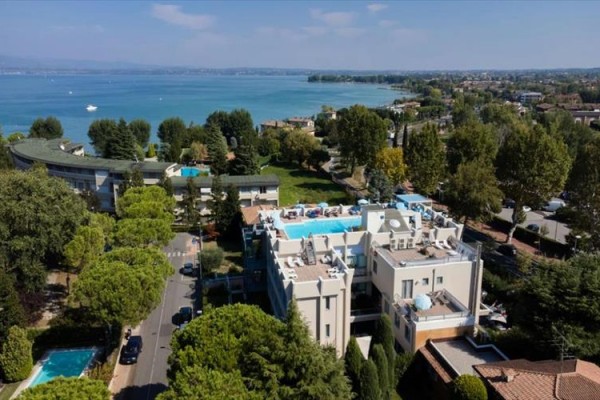 Pohled na hotel s bazénem na střeše u jezera obklopený stromy a dalšími budovami.  