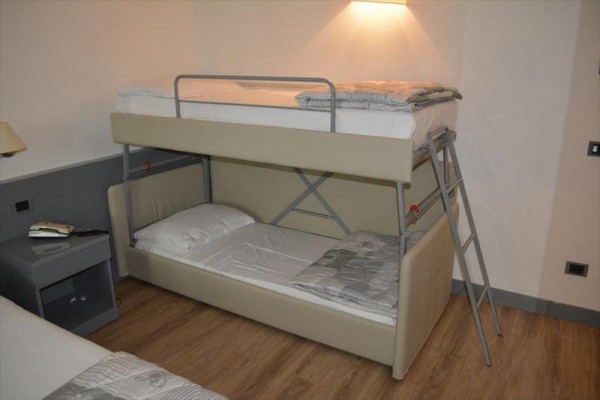 Patrová postel s dřevěnou podlahou a nočním stolkem vedle.