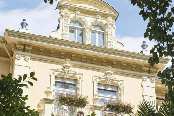 Historická budova s bohatou ornamentální fasádou a květinovou výzdobou na balkonech.