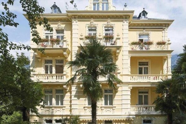 Historická budova se žlutou fasádou obklopená palmami.