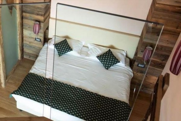 Ložnice s manželskou postelí, zelenými polštáři a dřevěnými obklady na stěnách.