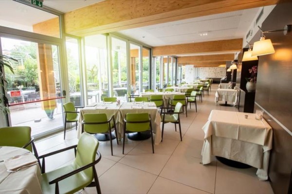 Moderní restaurace s prosklenými stěnami a zelenými židlemi.