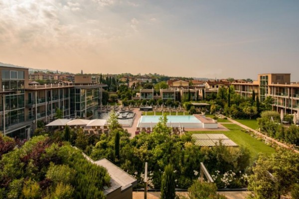Hotelový komplex s bazénem obklopený zelení a moderními budovami.