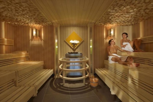 Sauna s dřevěnými lavicemi a lidmi relaxujícími uvnitř.