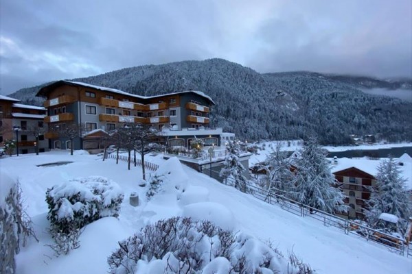 Horský hotel obklopený zasněženou krajinou a lesy.