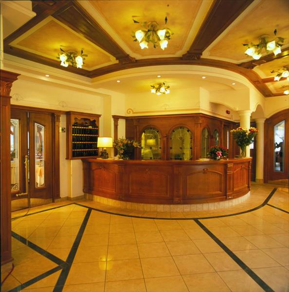 Recepce hotelu s dřevěným pultem a květinovou výzdobou.