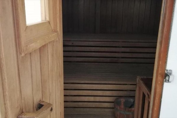 Otevřená dřevěná sauna s lavicí a malým vědrem uvnitř.